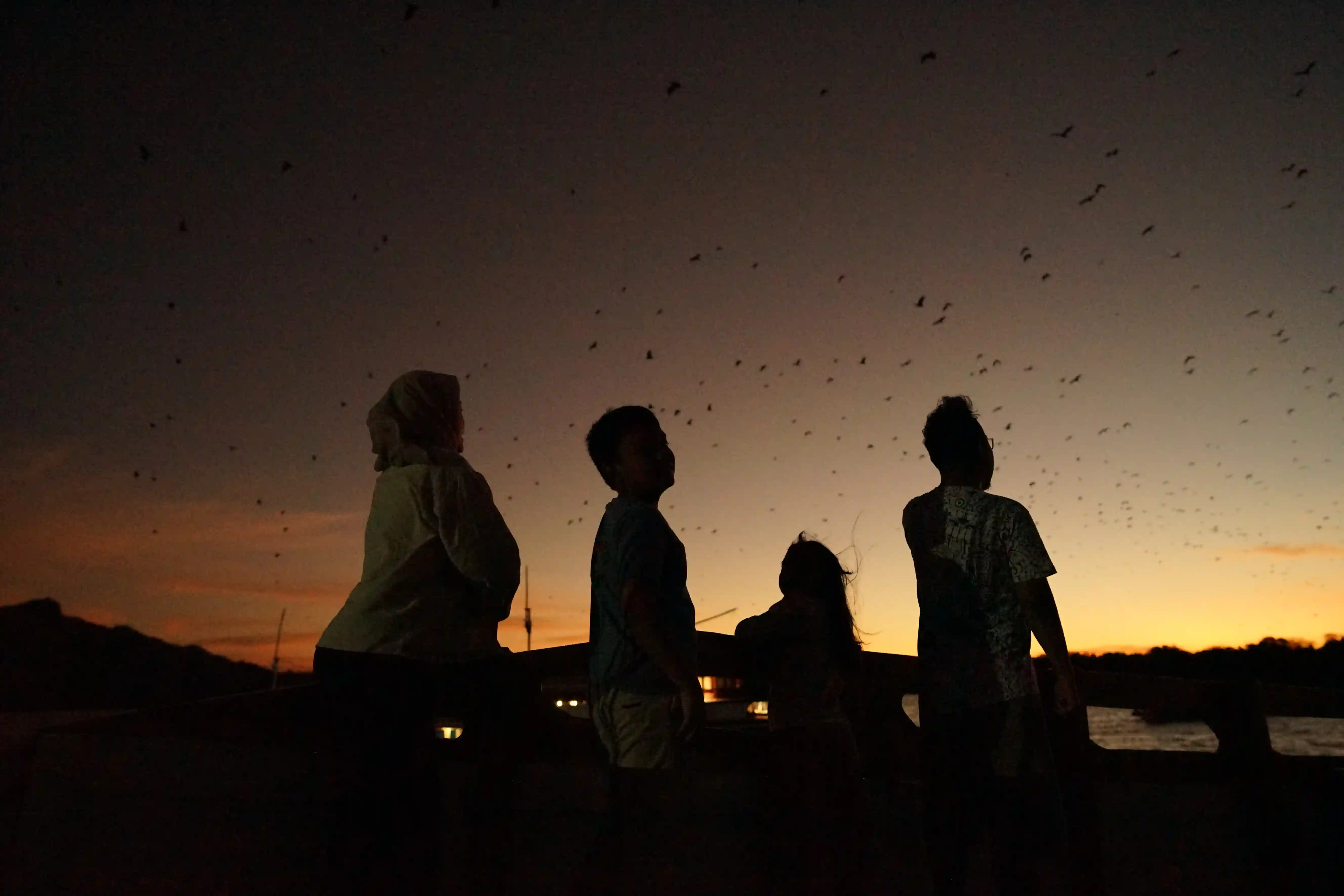 Travelers silhouetted at a golden-hour sunset viewpoint in the Komodo archipelago