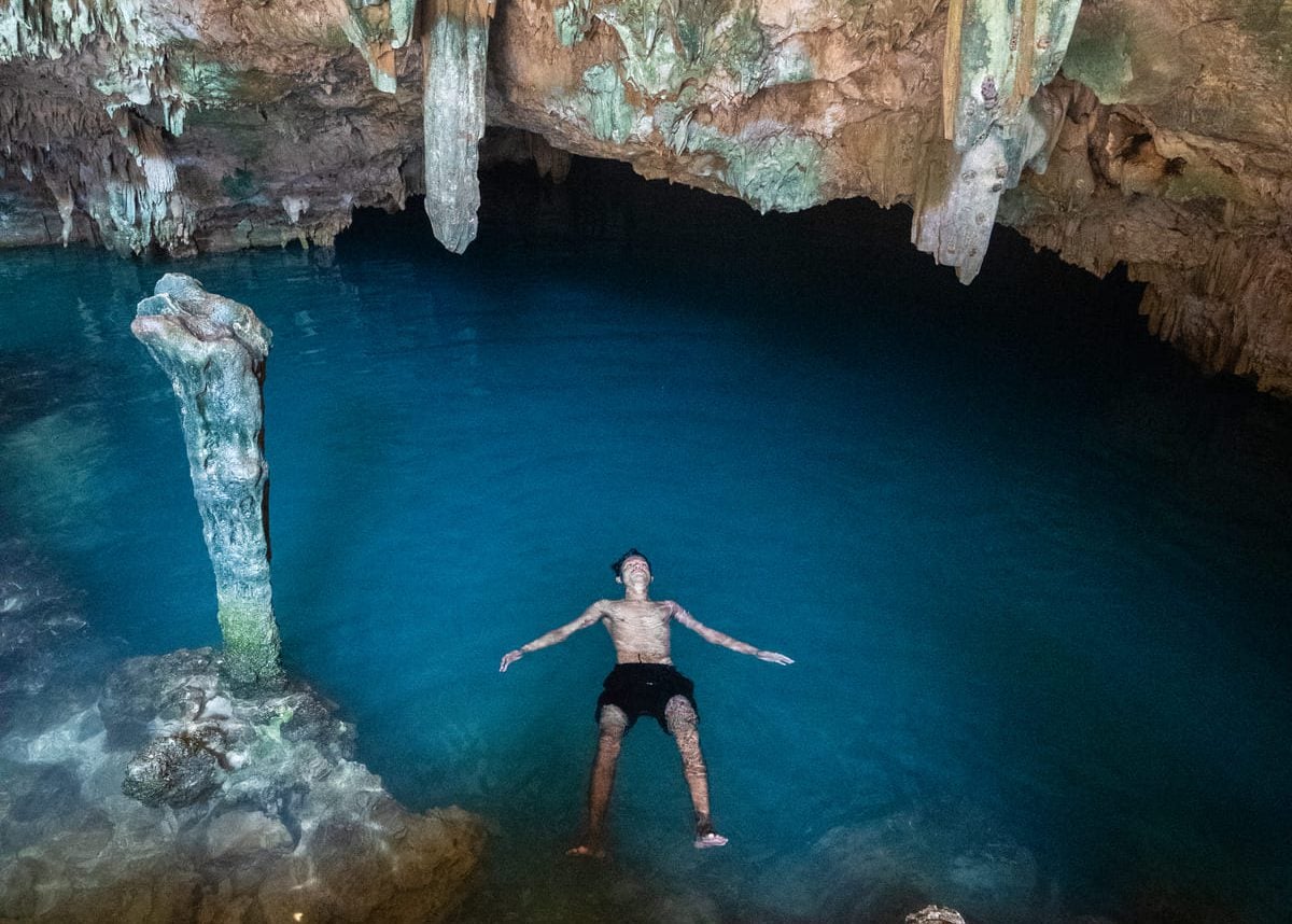 Swimmer suspended in clear blue water with light from the surface above