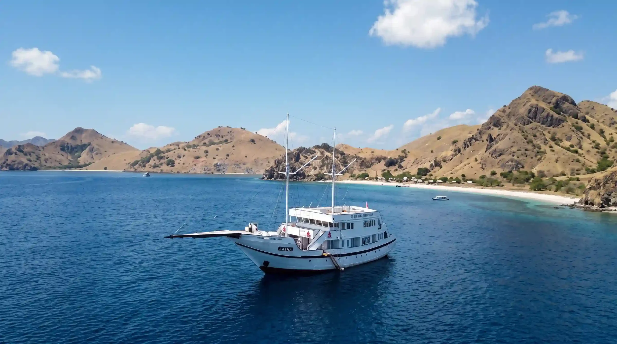 Lasha Phinisi Cruise anchored off a Komodo Island beach with dry savannah hills behind